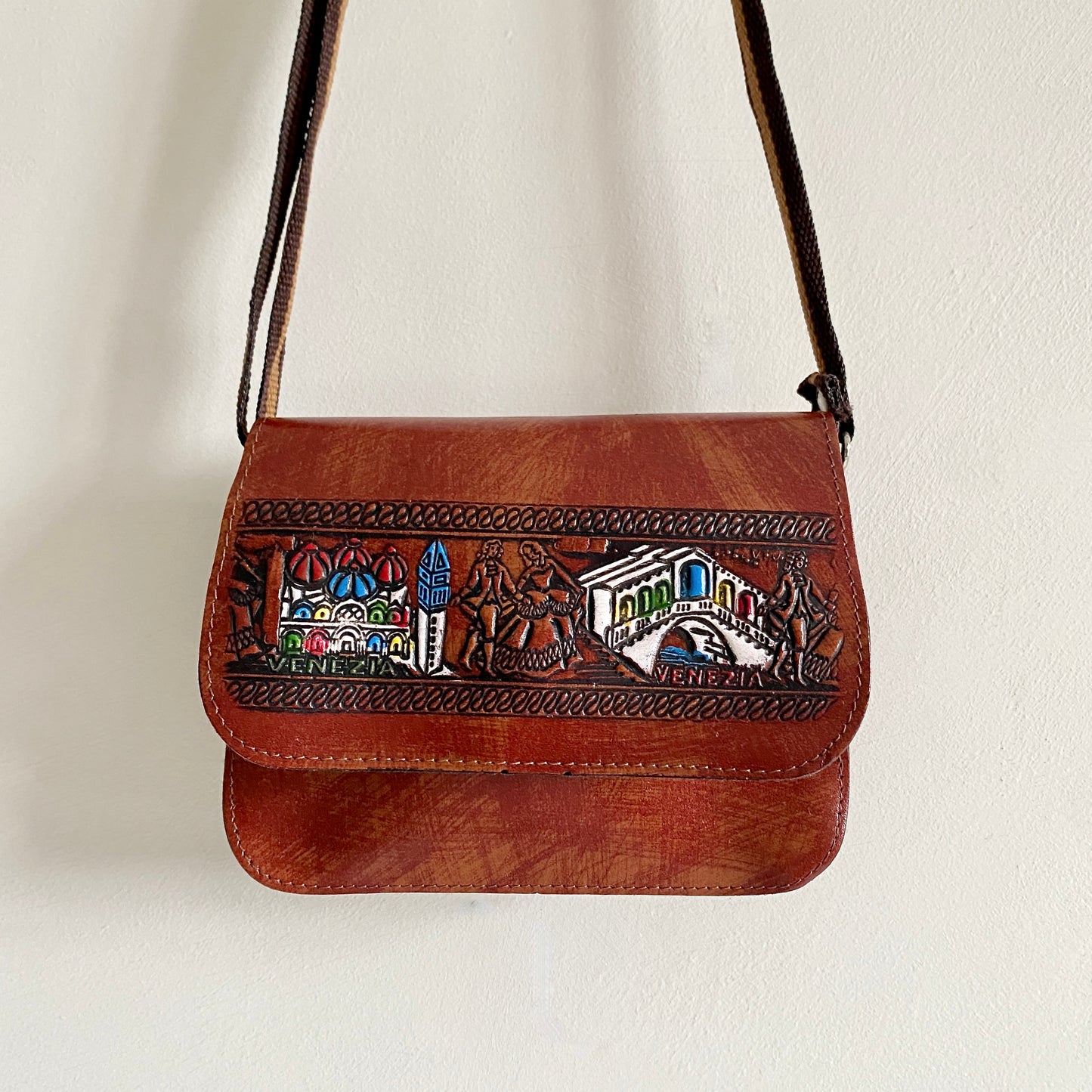 Vintage tan Venice 'tourist' bag Flap with press stud closure Hand tooled and hand painted detailing to front and back Adjustable fabric strap (measures 28"- 55") Two internal pockets with credit card slots Regenerated Leather Made in Italy
