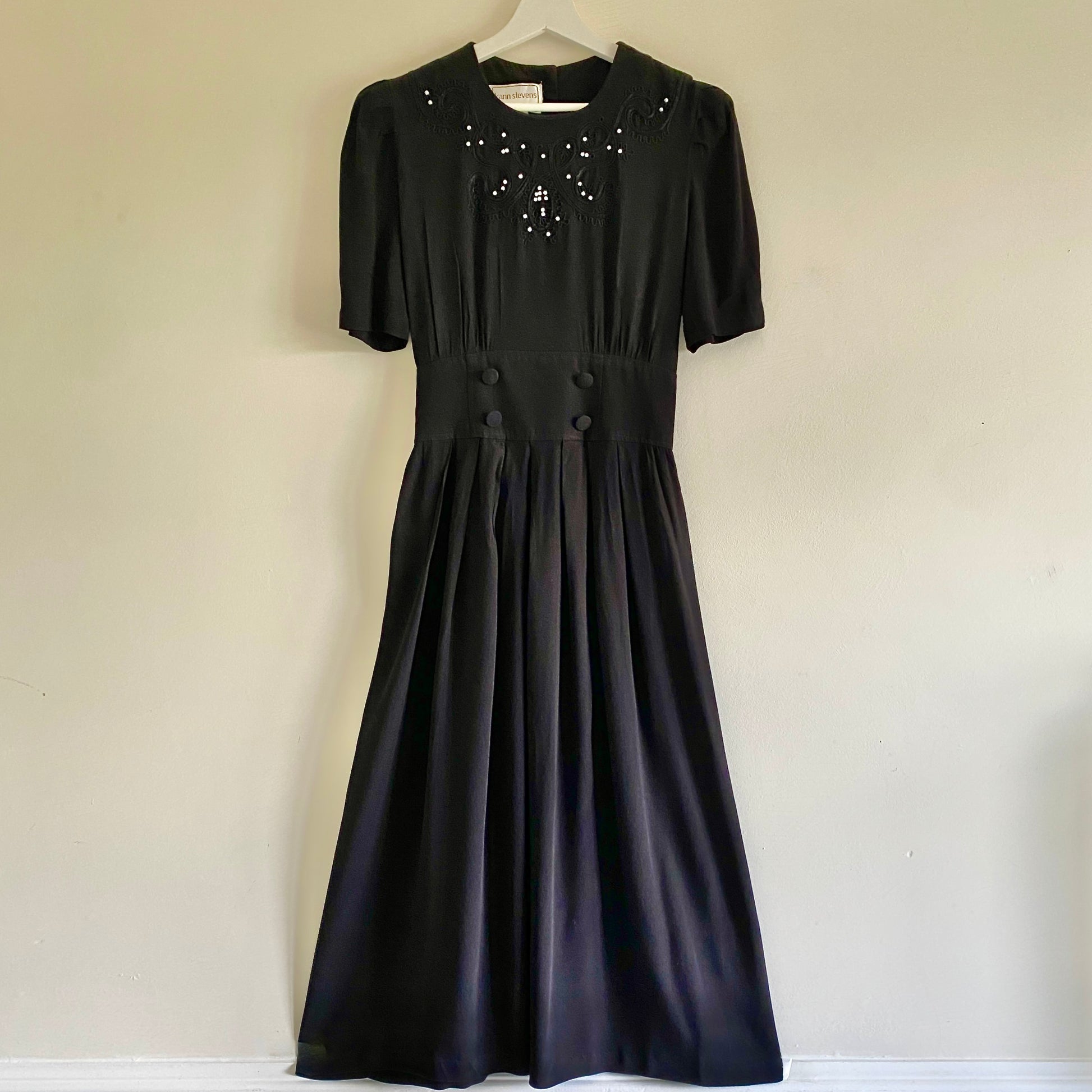 80s vintage black midi dress Decorative braiding and beads to front Short sleeves with gentle gathering to shoulders Button & zip fastening to back  Pleated skirt with elasticated back 4 decorative buttons to front waistband
